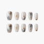 Set of marble-inspired press-on nails with gold foil and subtle grey, blue, and beige swirls.