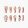 Handmade nude press-on nails with white floral designs, 3D butterfly and gem accents, and glitter.