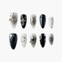 Black and white handmade press-on nails with metallic 3D charms, abstract and celestial designs.