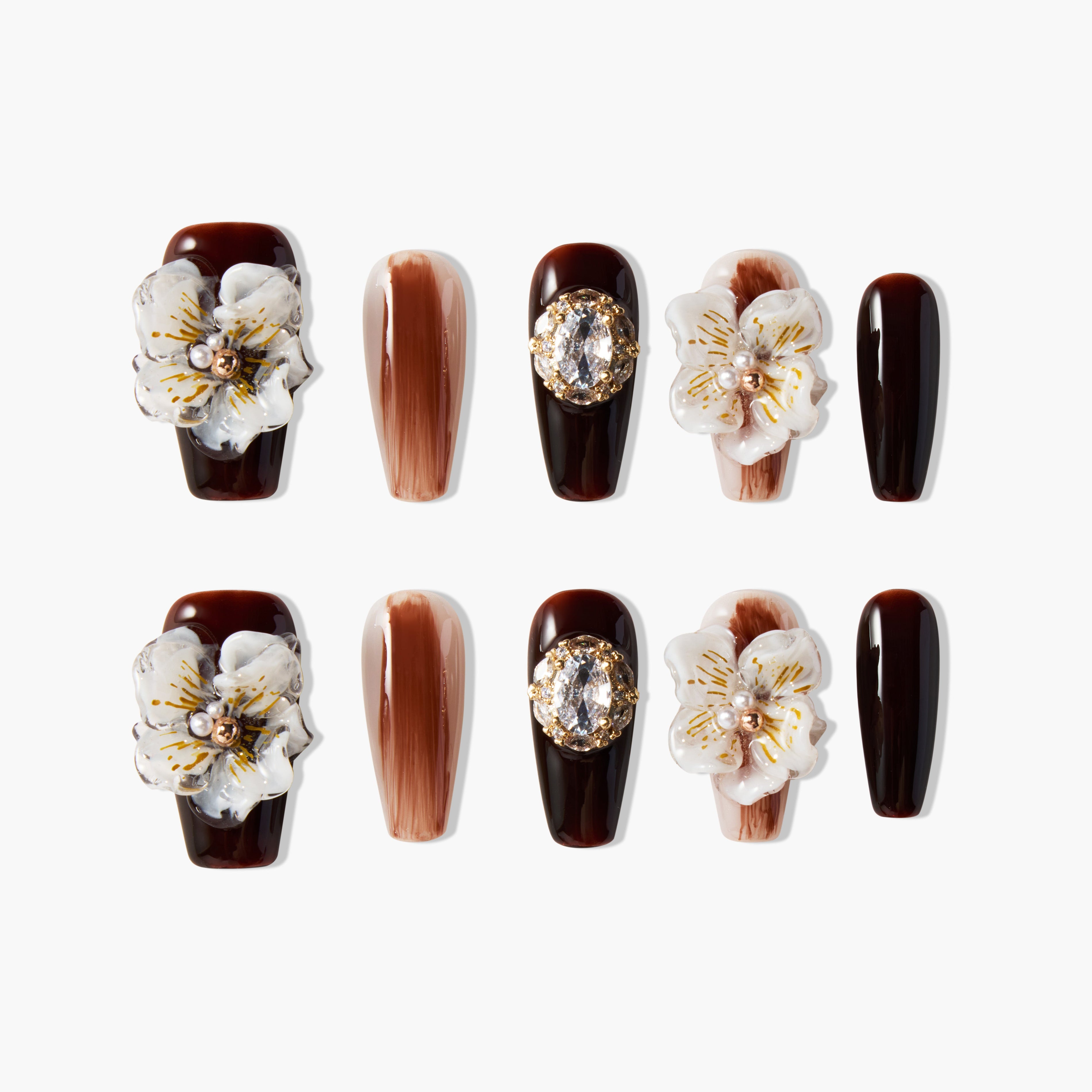 Brown press-on nails with 3D white floral accents, gold gems, and marble design details.