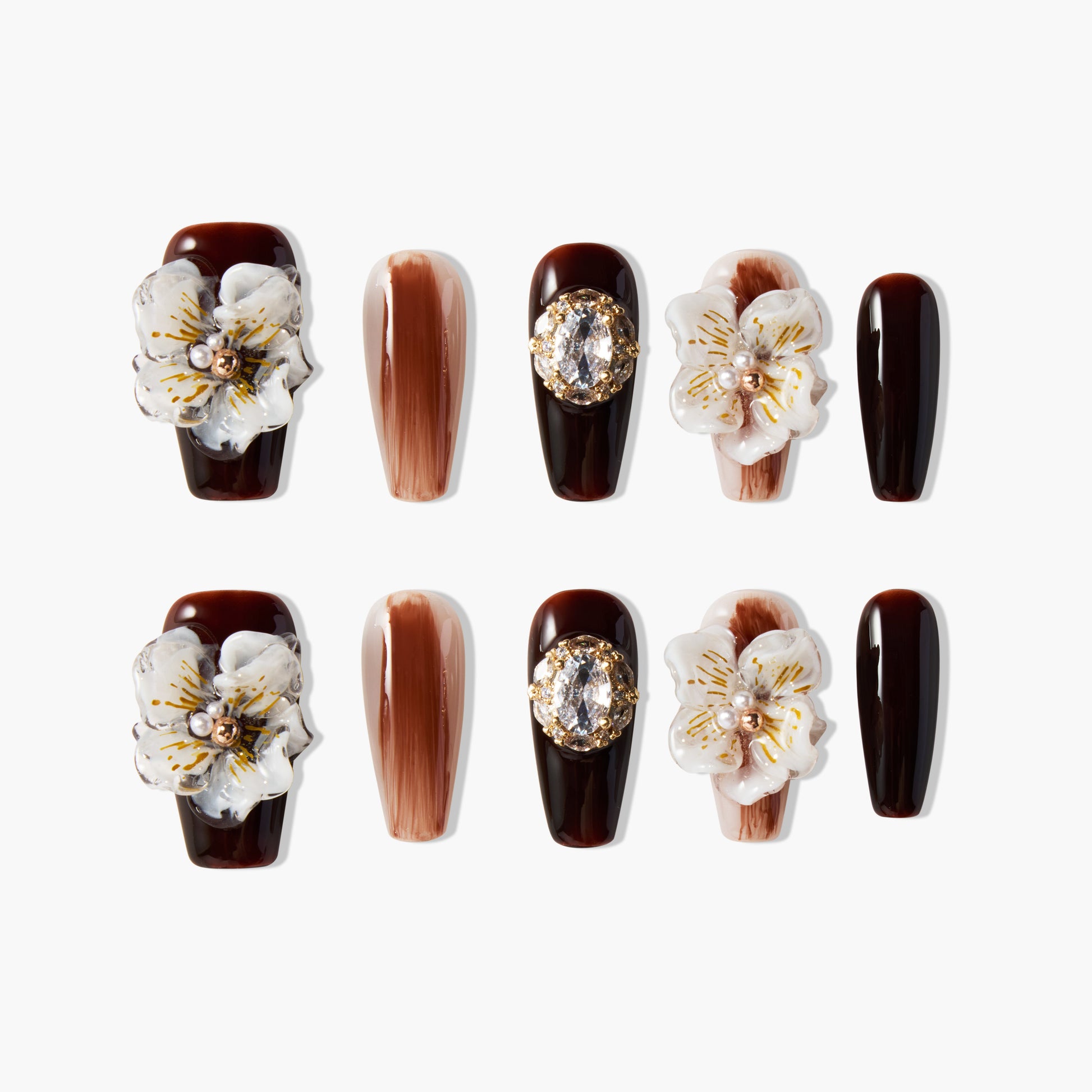 Brown press-on nails with 3D white floral accents, gold gems, and marble design details.
