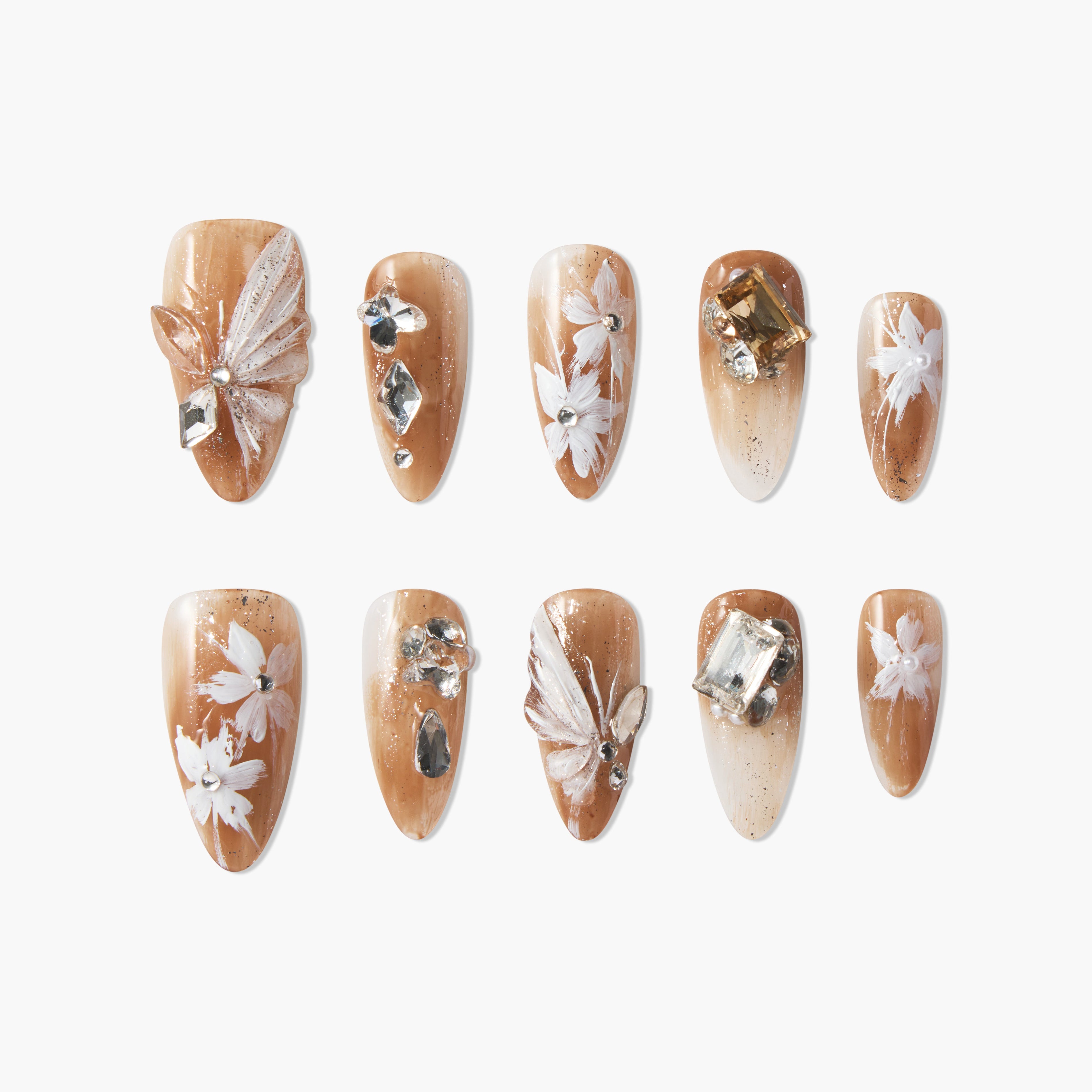 Handmade press-on nails with brown base, white floral designs, and rhinestone accents