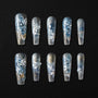 Handmade press-on nails with blue and white floral designs, gold accents, and pearl embellishments on a black background.