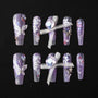 Handmade press-on nails with purple glitter, 3D butterfly, floral art, rhinestones, and ribbon accents.
