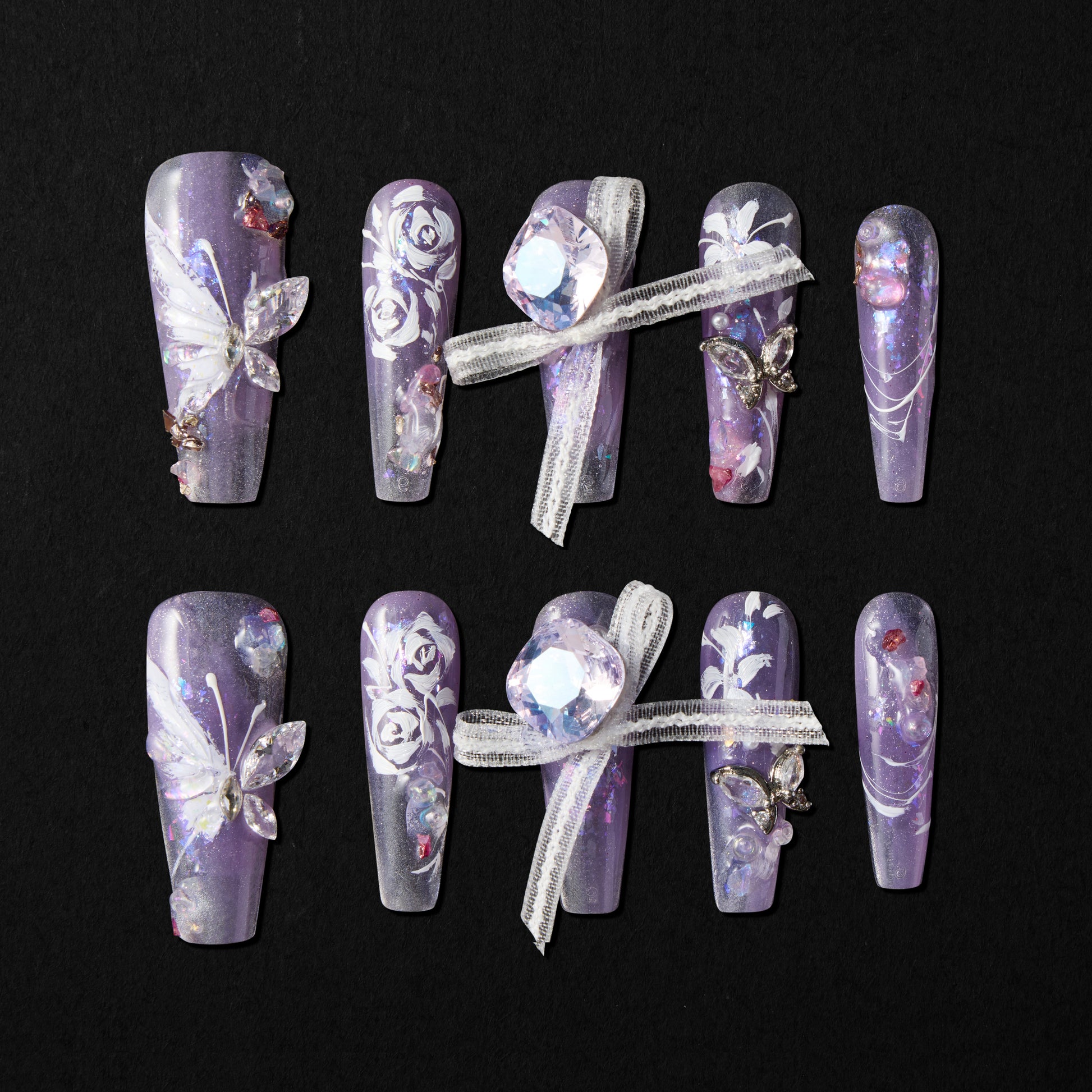 Handmade press-on nails with purple glitter, 3D butterfly, floral art, rhinestones, and ribbon accents.