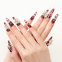 Red coffin-shaped press-on nails with 3D white floral and rhinestone accents, displayed on hands