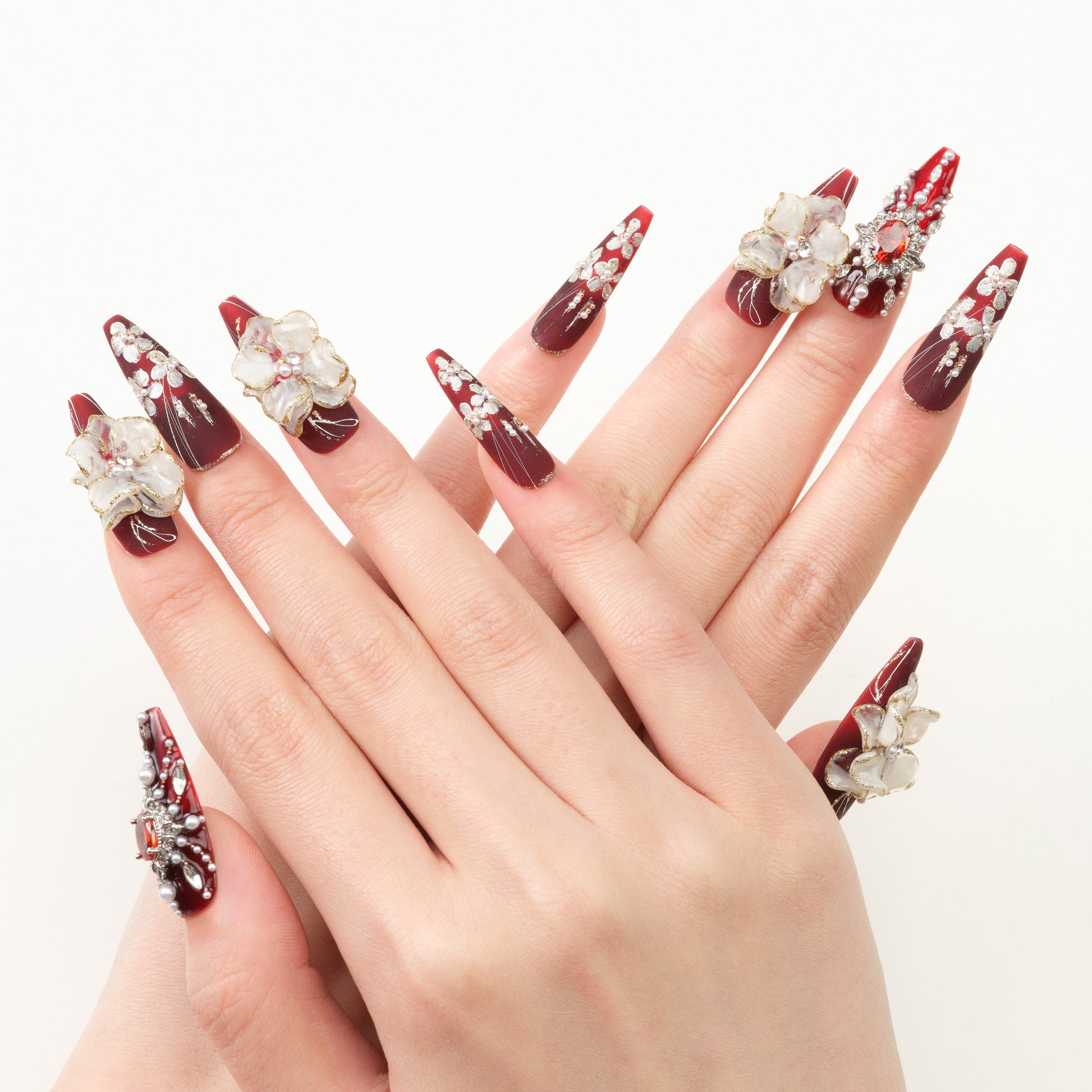 Red coffin-shaped press-on nails with 3D white floral and rhinestone accents, displayed on hands