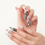 Hand with long stiletto press-on nails in pink, silver, and blue, adorned with gems and pearls