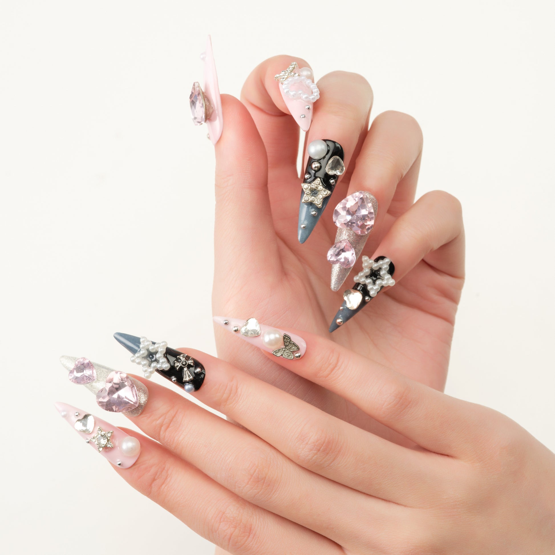 Hand with long stiletto press-on nails in pink, silver, and blue, adorned with gems and pearls