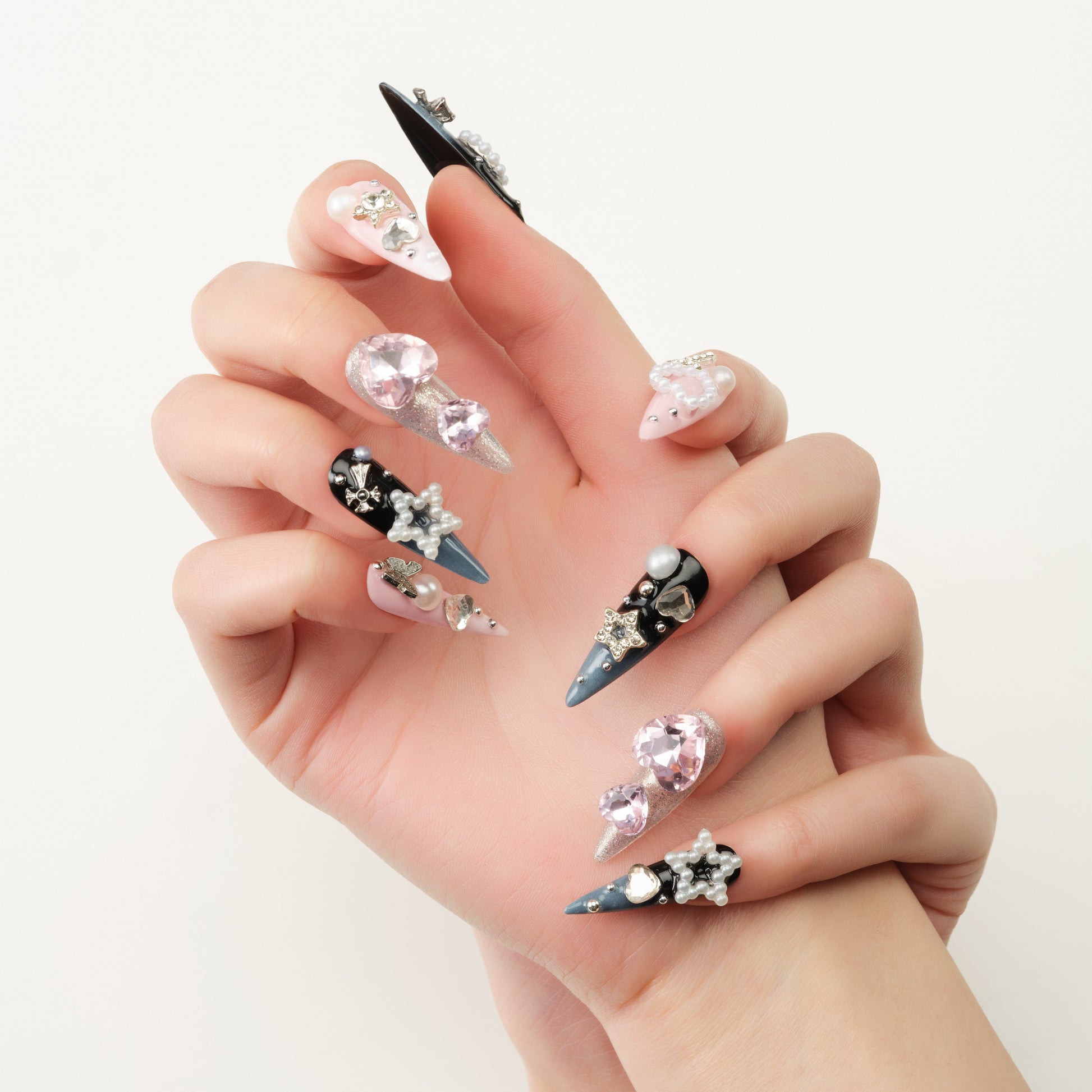 Hand with long press-on nails featuring 3D gems, pearls, stars, and black and blue accents