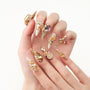 Hand with long press-on nails featuring 3D gold charms, crystals, and rose embellishments.