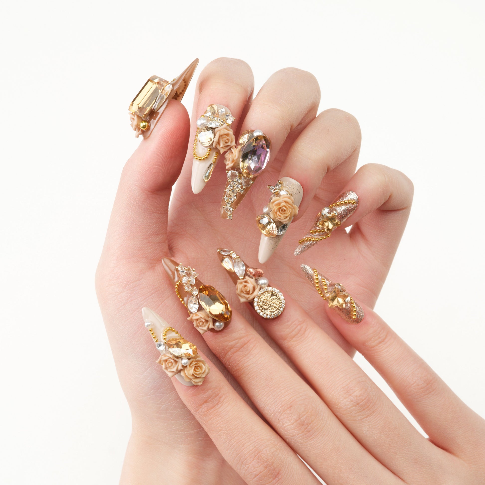Hand with long press-on nails featuring 3D gold charms, crystals, and rose embellishments.
