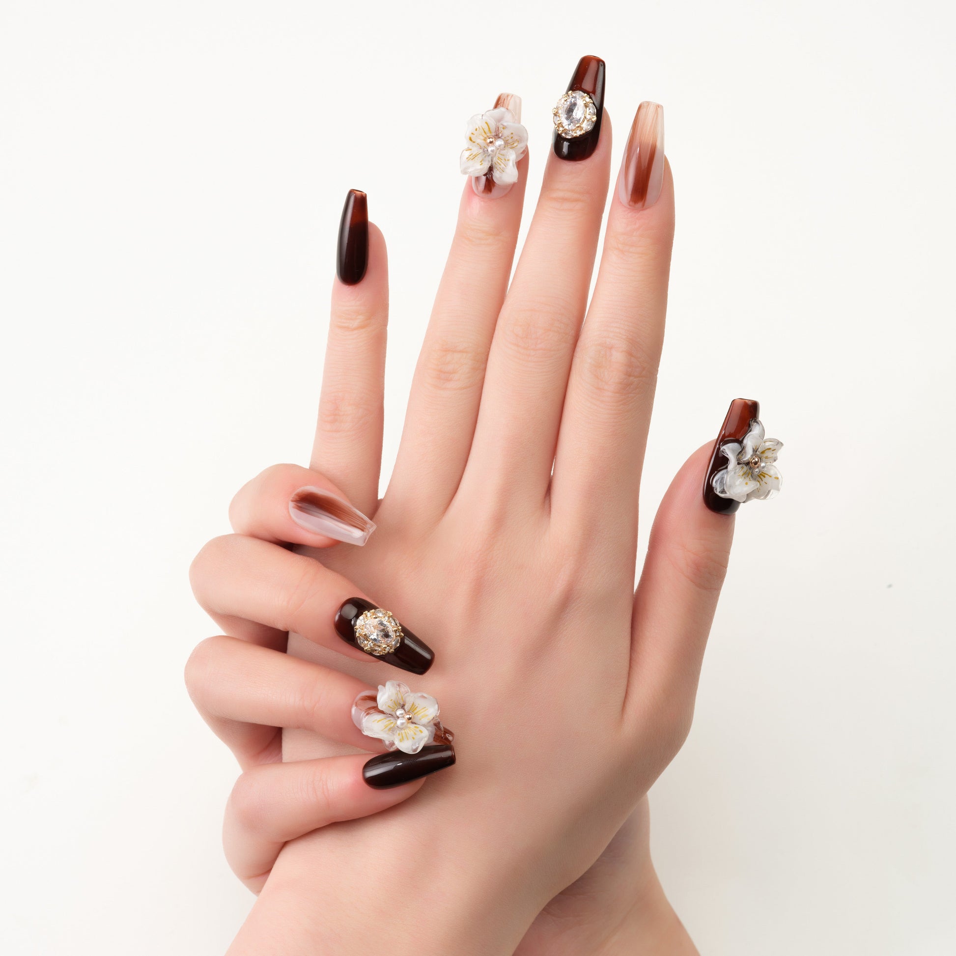 Hand with brown and nude press-on nails, 3D floral accents and rhinestone designs