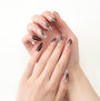 Hand with long almond-shaped press-on nails in black and nude with intricate floral designs