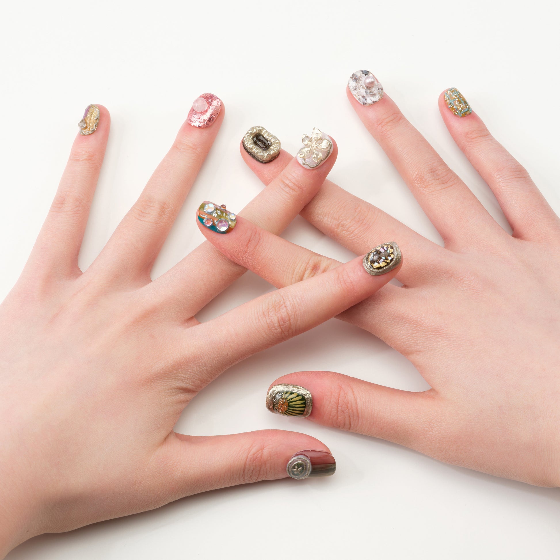 Hands with premium handmade press-on nails featuring 3D gems, pearls, and glitter designs.