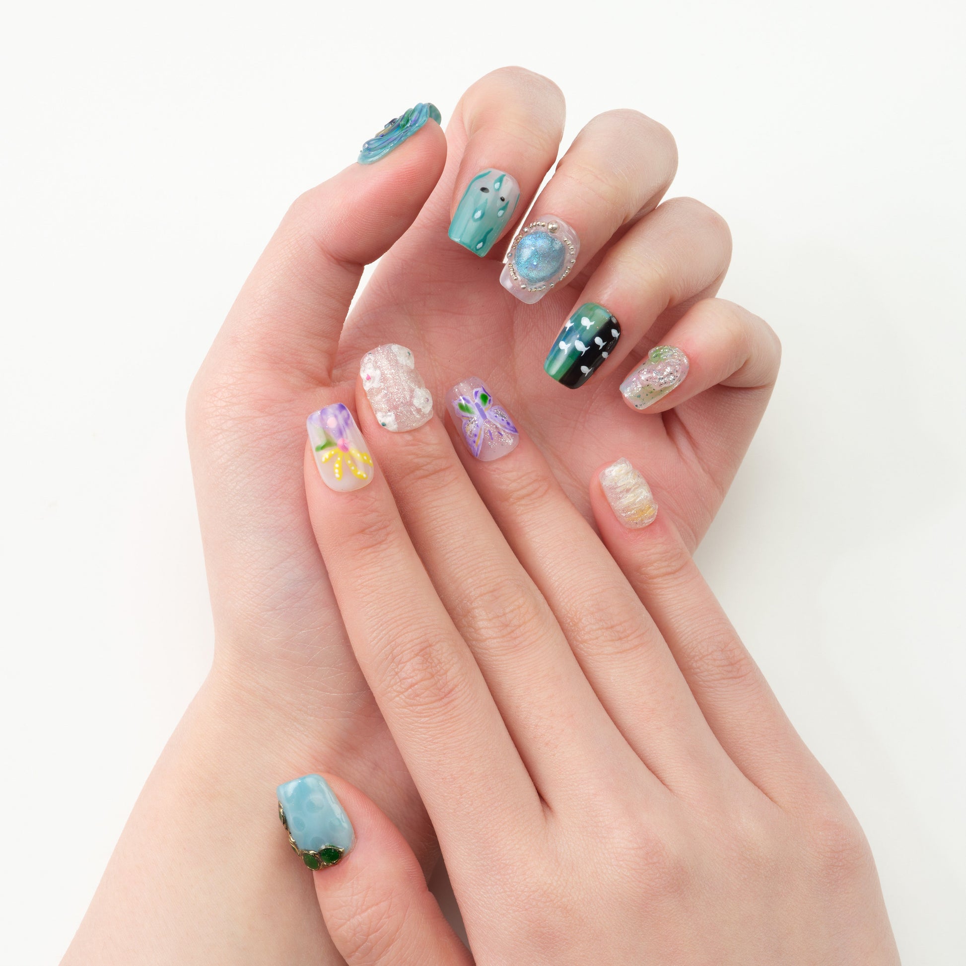 Hand with colorful handmade press-on nails featuring floral, gemstone, and abstract nail art designs