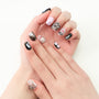 Hand with black and pink press-on nails featuring floral and bow designs, on white background