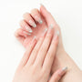 Hand with long almond-shaped press-on nails featuring silver glitter and rhinestone accents