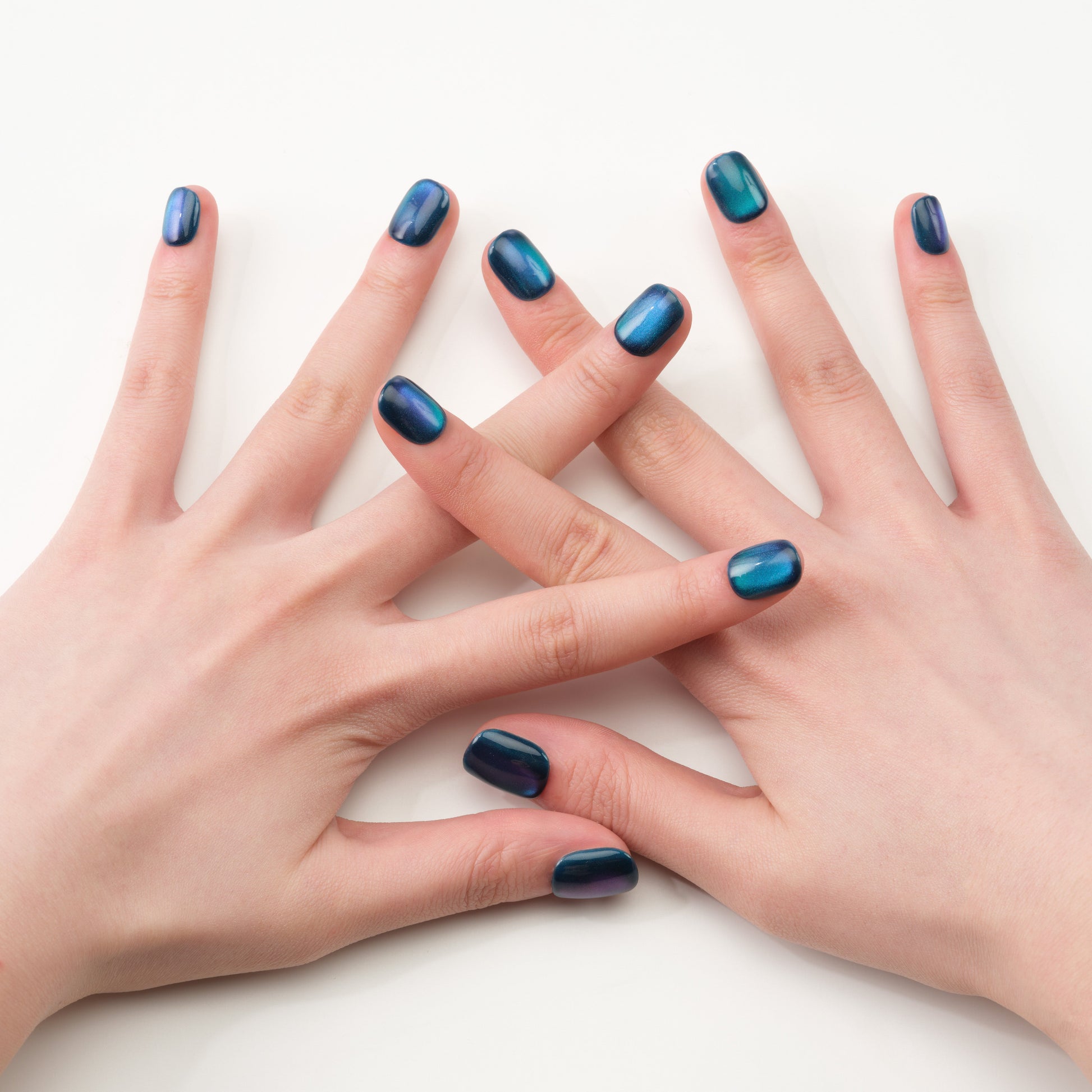 Hands with glossy blue green chrome press-on nails on a white background