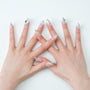 Hands with long almond-shaped press-on nails, silver ombre tips, and 3D jewel accents.
