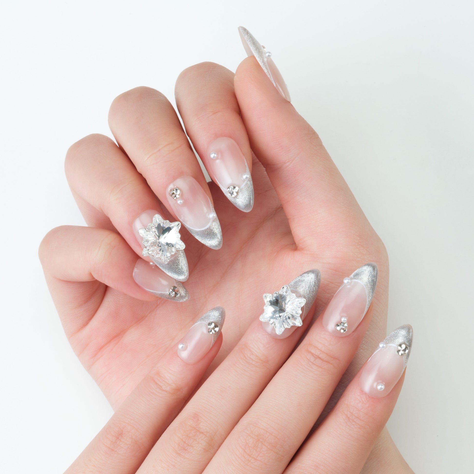 Hand with pointed silver French tip press-on nails, rhinestone and pearl nail art design