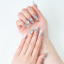 Hand with long silver press-on nails decorated with rhinestones and glitter on white background