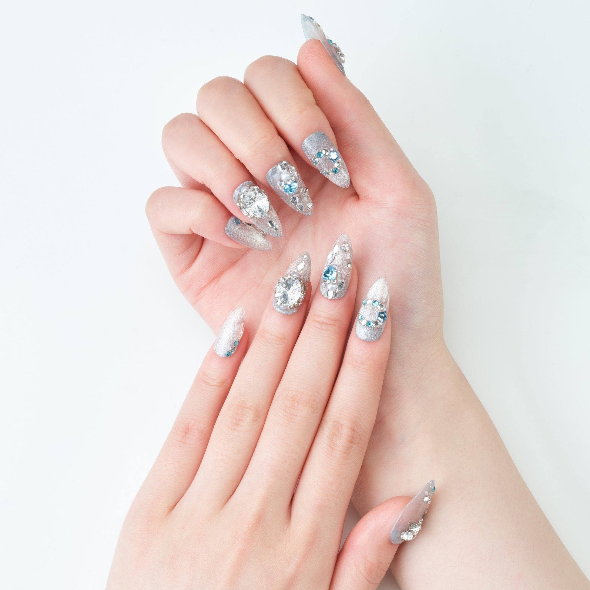 Hand with long silver press-on nails decorated with rhinestones and glitter on white background