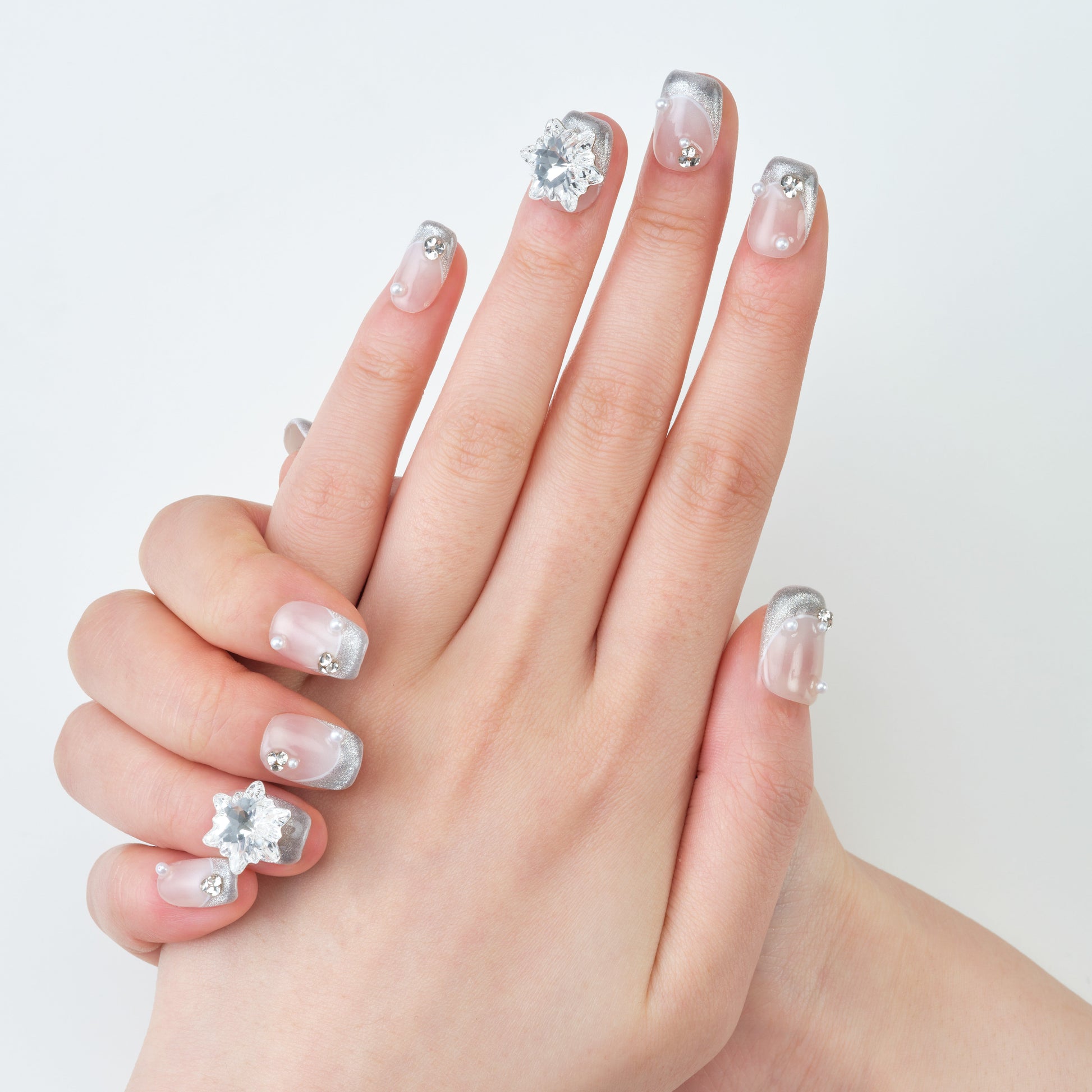 Hand with silver and clear handmade press-on nails featuring rhinestone and pearl accents