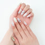 Hand with long almond-shaped press-on nails featuring white, pastel, and rhinestone nail art