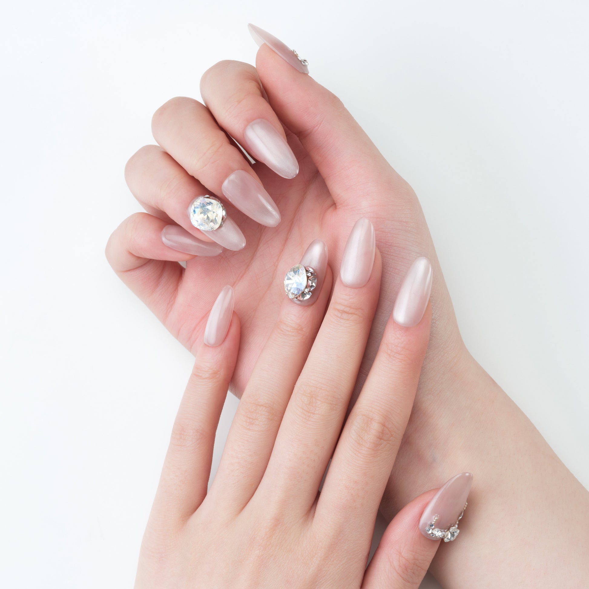 Hand with almond-shaped nude press-on nails, accent nails feature large rhinestones.