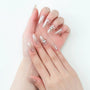 Hand with almond-shaped nude press-on nails and accent gemstone nail art on a white background