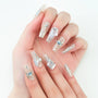 Hand with long clear press-on nails decorated with blue gems, crystals, and butterfly accents