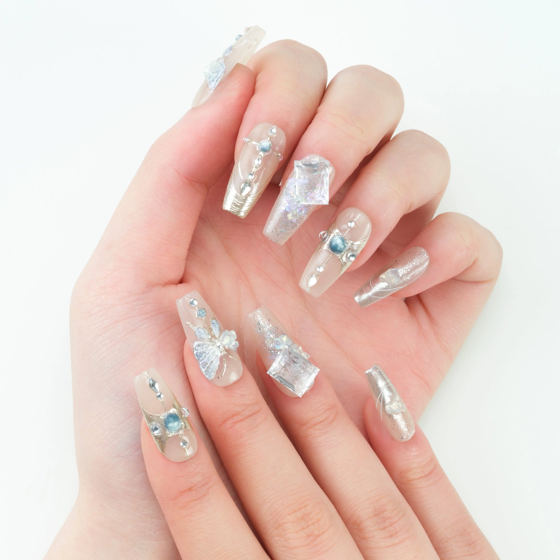Hand with long clear press-on nails decorated with blue gems, crystals, and butterfly accents