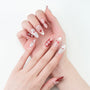 Hand with long, red and white almond-shaped press-on nails, adorned with jewels and cherry art.