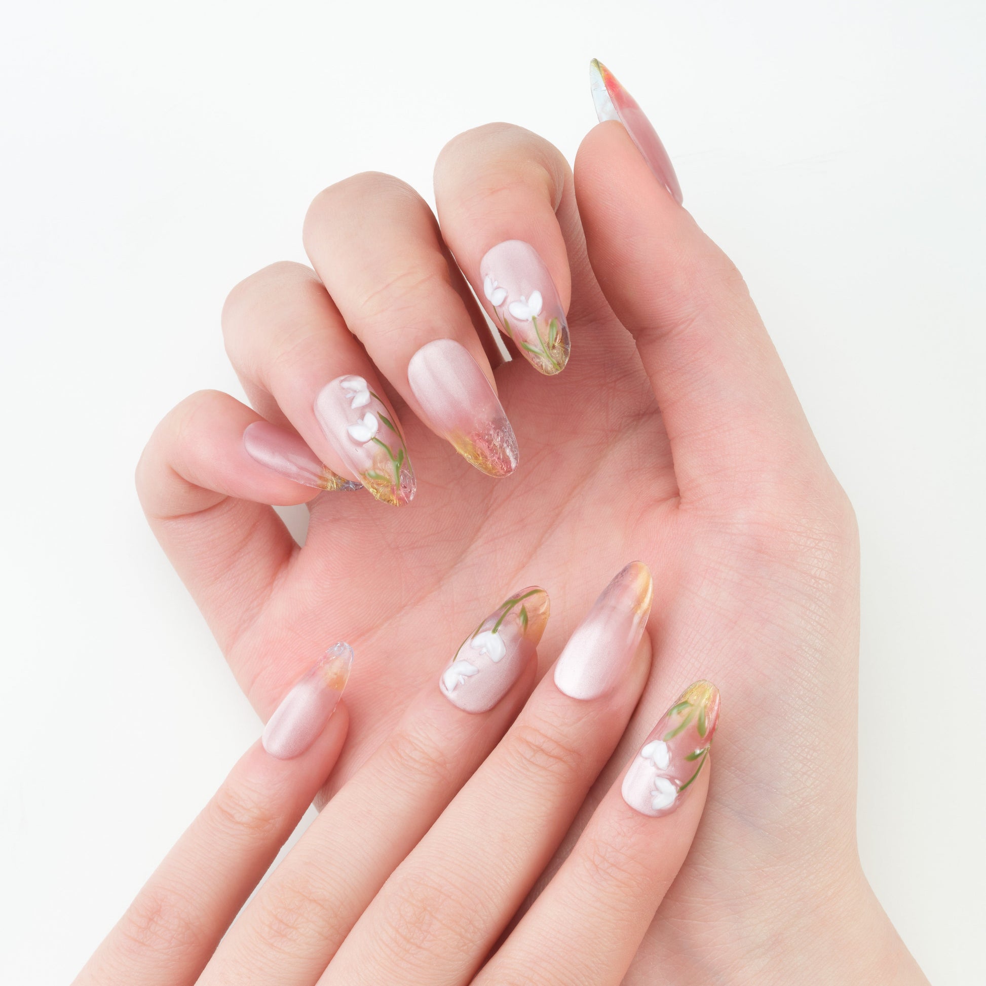 Hand with long almond-shaped press-on nails featuring pink ombre and white floral designs