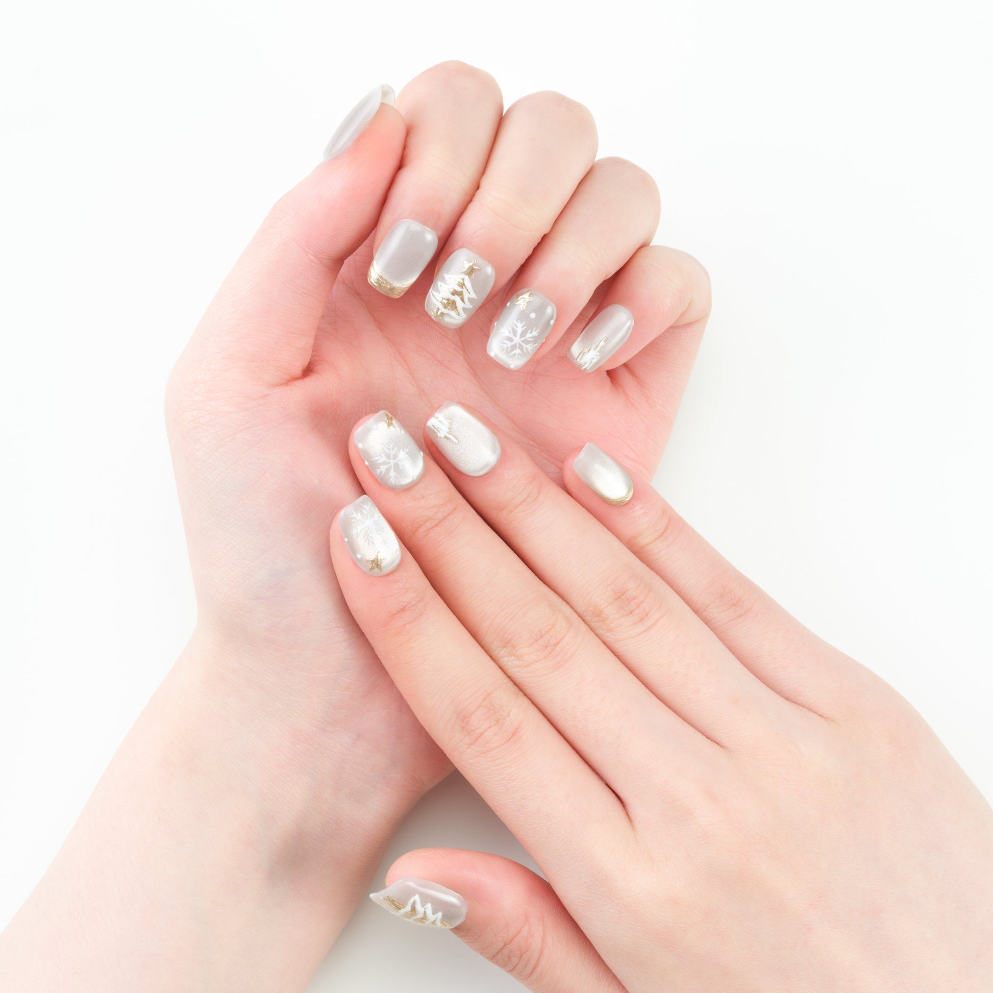 Hand with silver press-on nails featuring snowflake and tree winter nail art designs