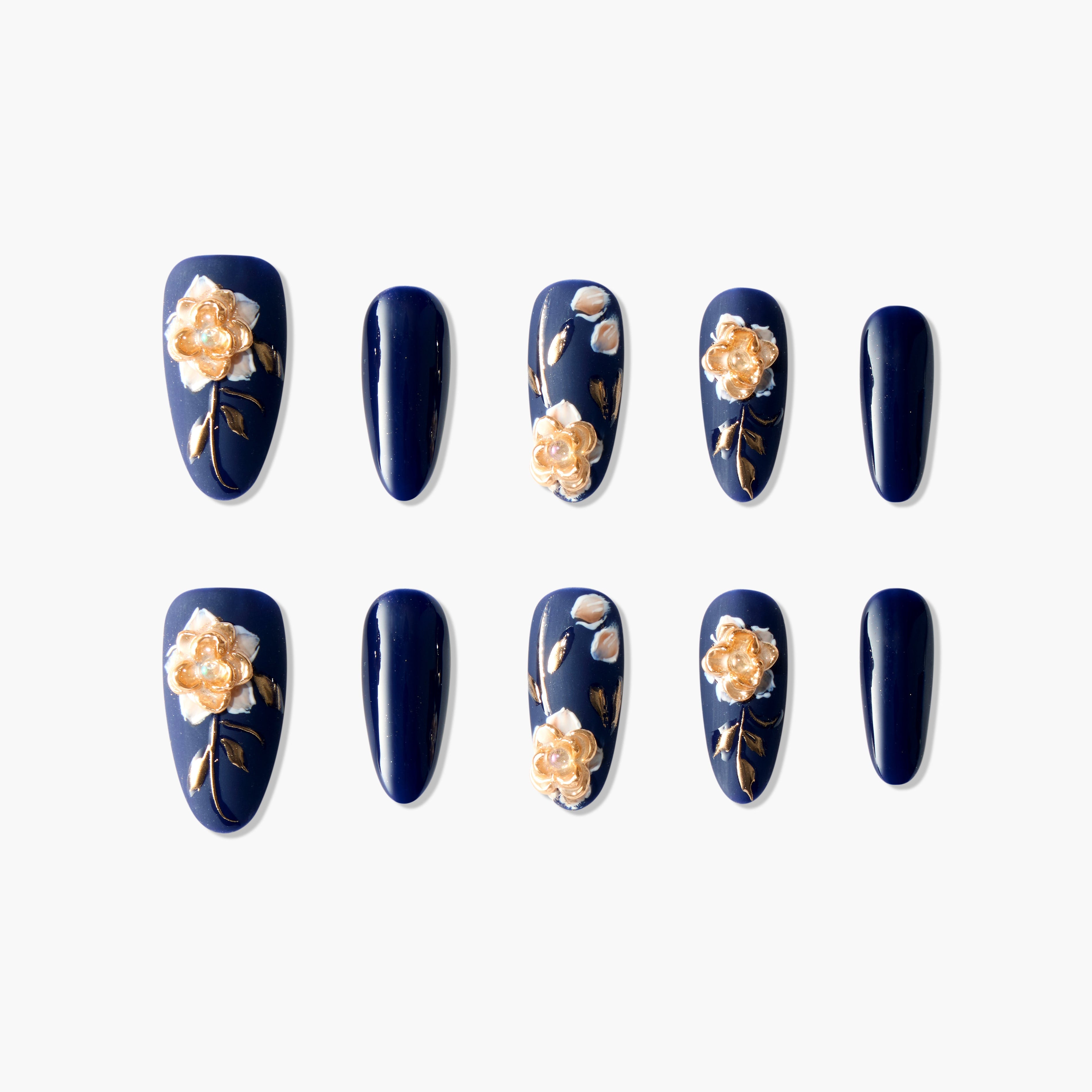 Navy blue press-on nails with gold 3D floral and leaf designs, arranged on white background.