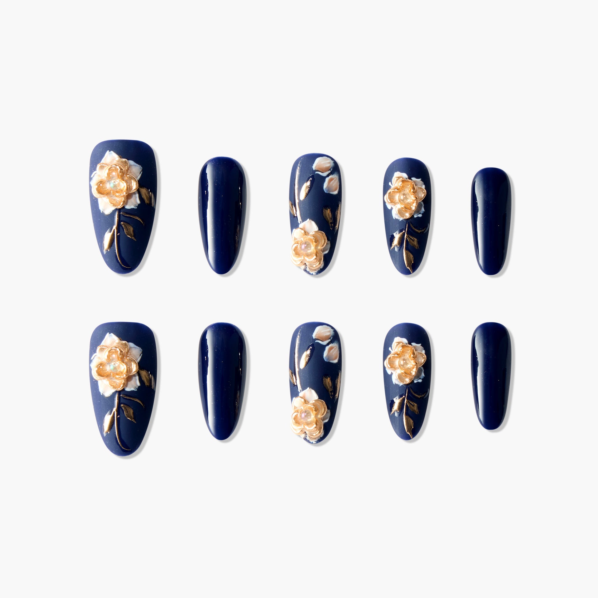 Navy blue press-on nails with gold 3D floral and leaf designs, arranged on white background.