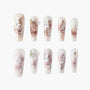 Handmade press-on nails with white floral designs, rose gold foil, and shimmery accents