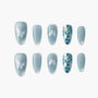 Blue press-on nails with iridescent butterfly designs and blue glitter accents, arranged on white background.
