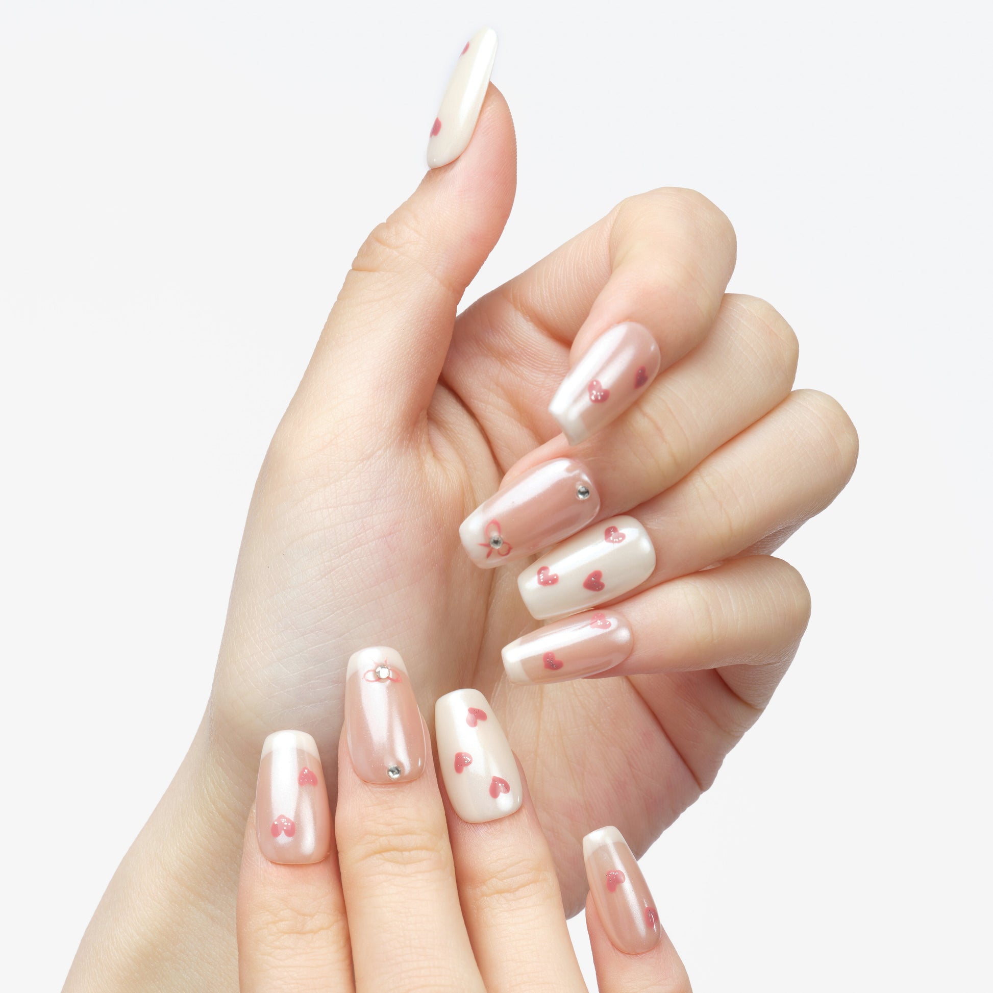 Hand with long press-on nails featuring pink heart nail art and rhinestone accents.