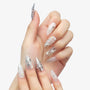 Hand with long stiletto press-on nails in silver and nude, adorned with 3D stars, pearls, and rhinestones