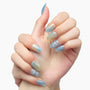 Hand with iridescent blue and gold gradient press-on nails, oval shape, on white background.
