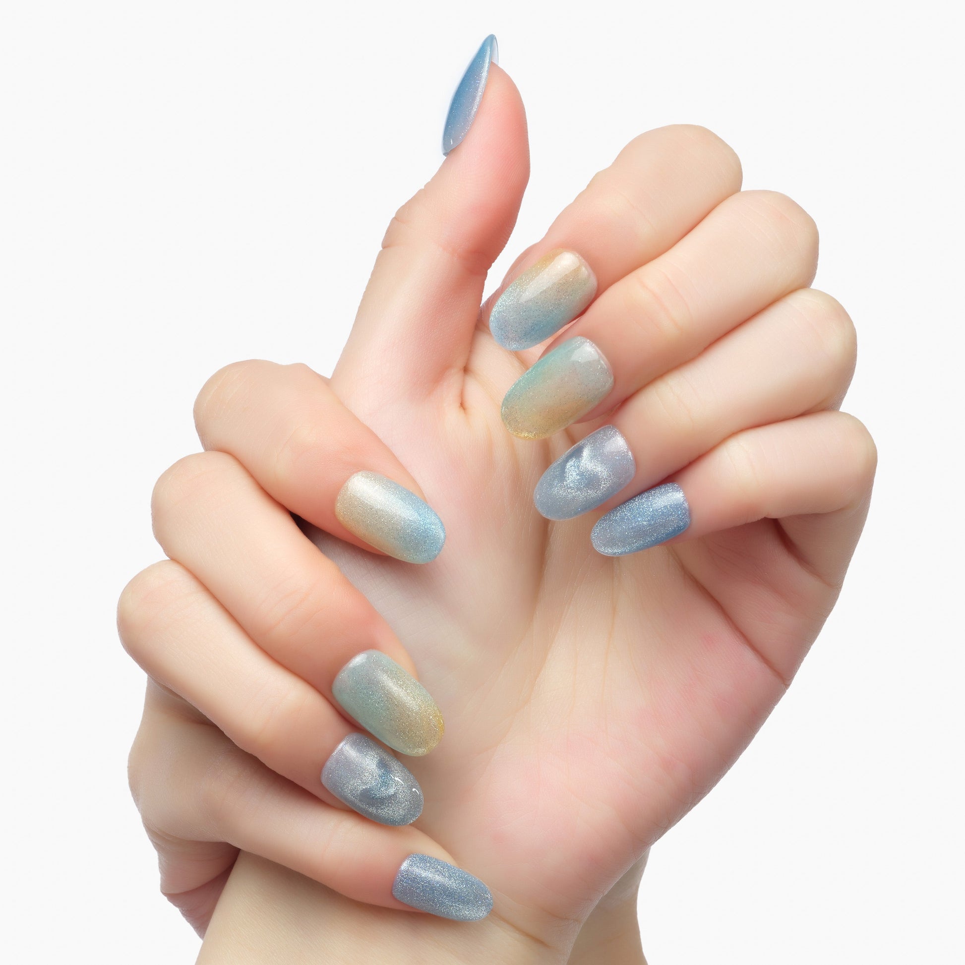 Hand with iridescent blue and gold gradient press-on nails, oval shape, on white background.