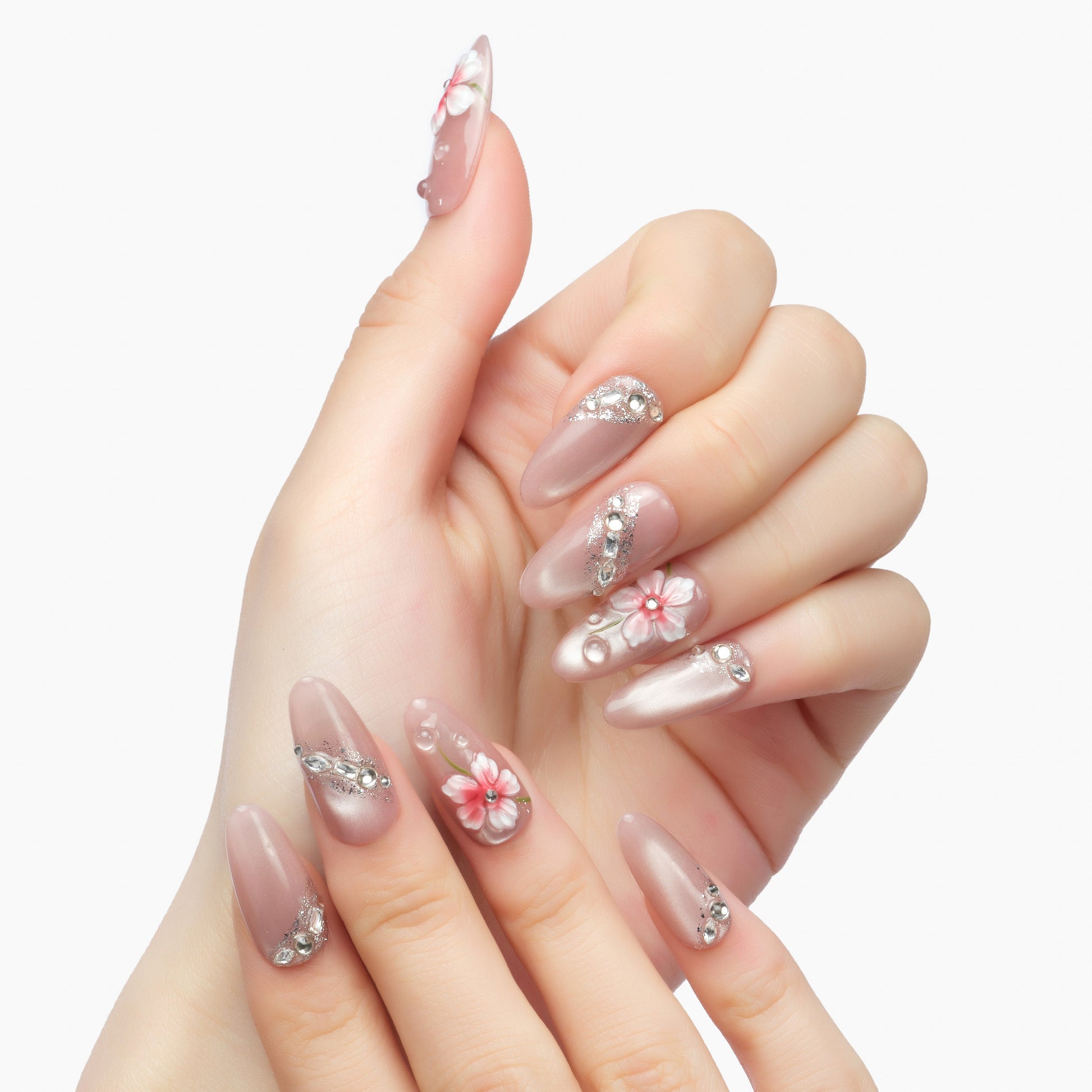 Hand with long almond-shaped press-on nails, featuring pink floral 3D designs and rhinestones