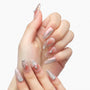 Hand with long, iridescent press-on nails featuring 3D floral designs and rhinestones