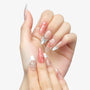 Hand with long almond-shaped press-on nails in pink, white, and clear designs with metallic bows and gems