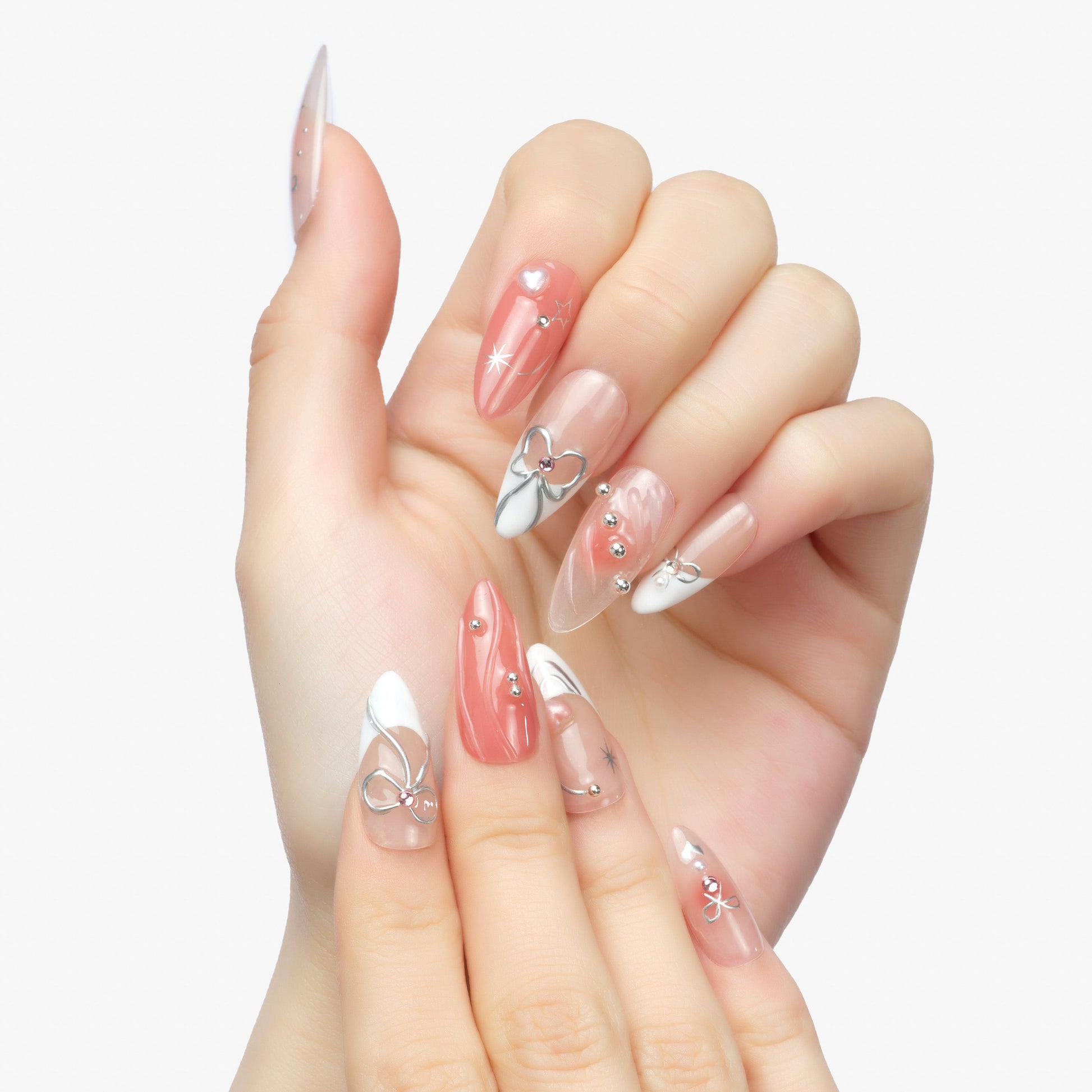 Hand with long almond-shaped press-on nails in pink, white, and clear designs with metallic bows and gems