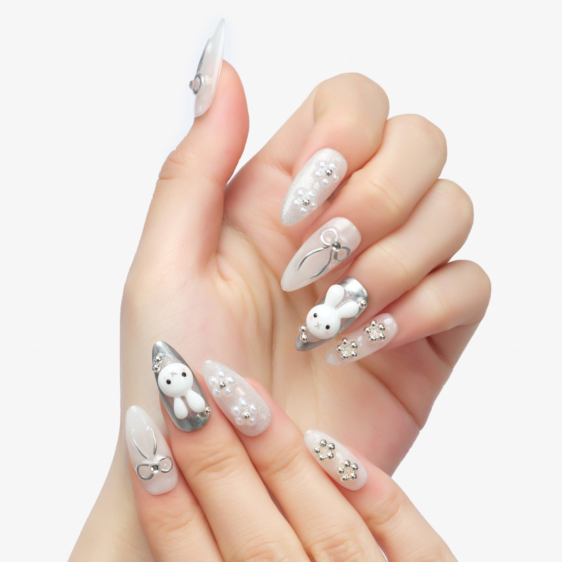 Hand with long almond-shaped press-on nails featuring 3D bunny, pearls, bows, and silver accents