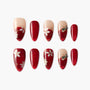 Red and nude floral press-on nails with gemstone accents and gold detailing, oval shape.